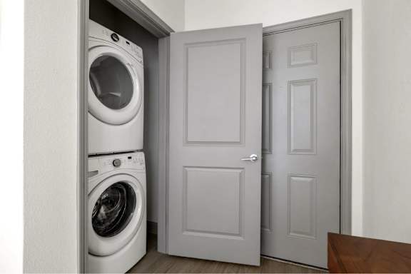 A white washing machine is in a small space between a door and a wall.