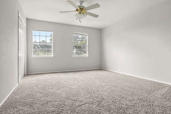 A room with a ceiling fan and two windows.