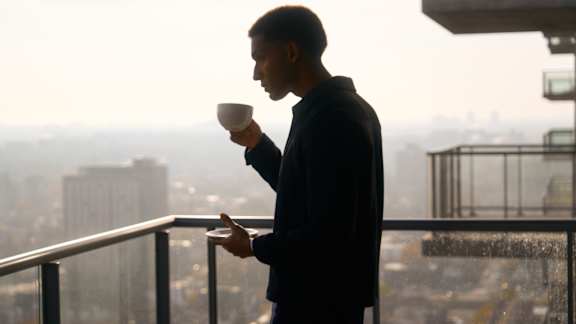 A man in a black jacket is standing on a balcony holding a white cup at The Dale Apartments , Ontario, K1Y 4Y5