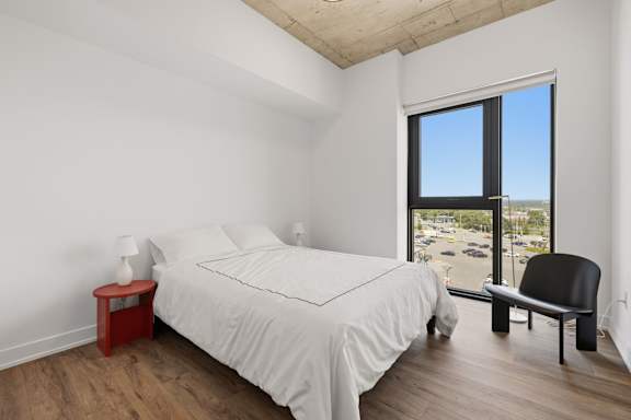 A bedroom with a large bed, a chair, and a window overlooking a parking lot.