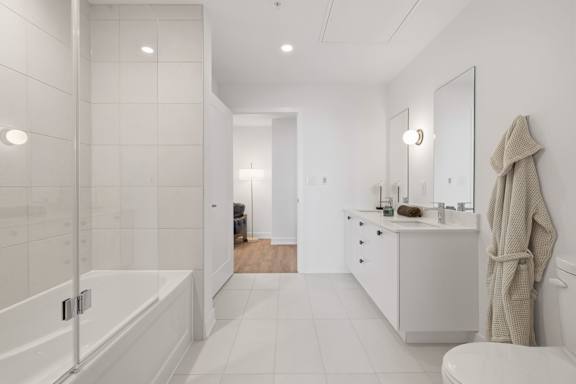 A white bathroom with a large mirror and a white bathtub.
