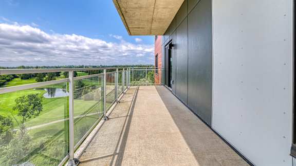 A balcony with a glass railing overlooking a green landscape. at Château golf, Gatineau