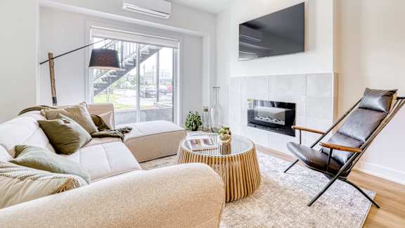 A living room with a white couch, a fireplace, and a television mounted on the wall.