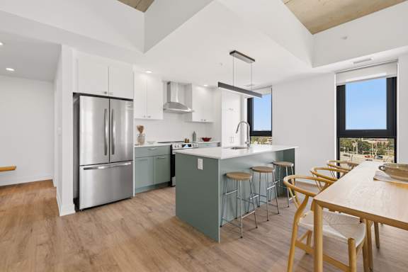 A modern kitchen with a refrigerator, stove, and bar stools.
