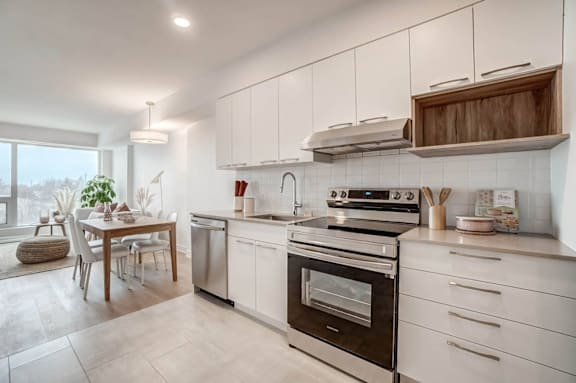 Modern kitchen with white cabinets and dining area at Baseline Apartments, Ottawa, ON