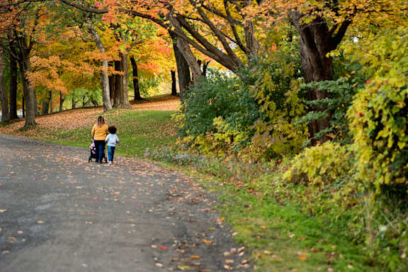 A woman and child walk down a leaf-covered path.