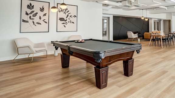 A pool table is in the middle of a room with a chair and a painting on the wall.