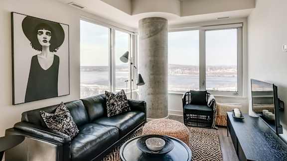 A living room with a black couch and a large window at The Dale Apartments , Ottawa