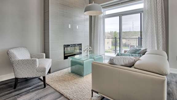 A modern living room with a white sofa, a glass coffee table, and a patterned chair.