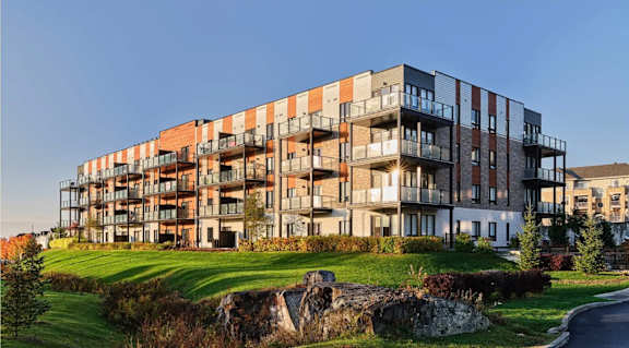 A large apartment building with balconies and a grassy area in front.