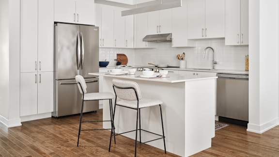 A kitchen with a white island and two chairs.