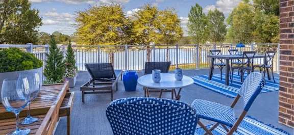A patio with blue chairs and a table with a glass of wine on it.