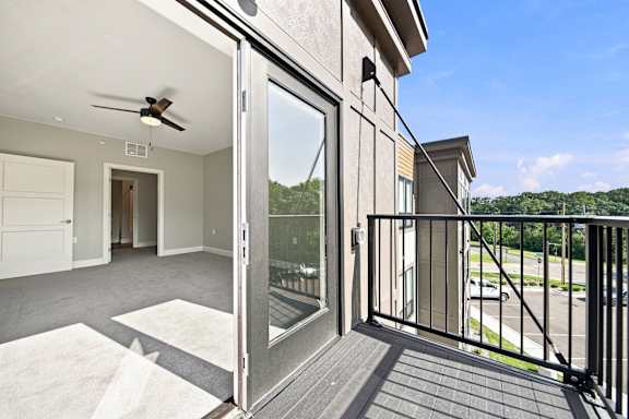 A balcony with a glass door leading to a room with a ceiling fan.