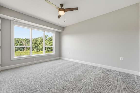 A room with a ceiling fan and a large window overlooking a green landscape.