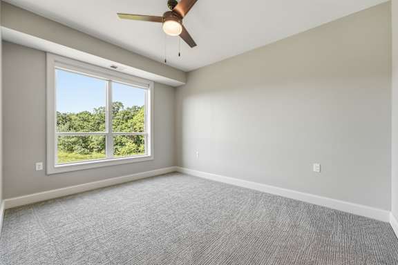 A room with a ceiling fan and a window overlooking a green landscape.