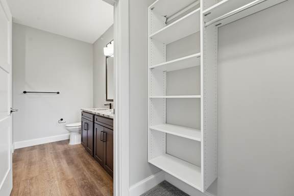 A white shelving unit is in a room with a toilet and sink.