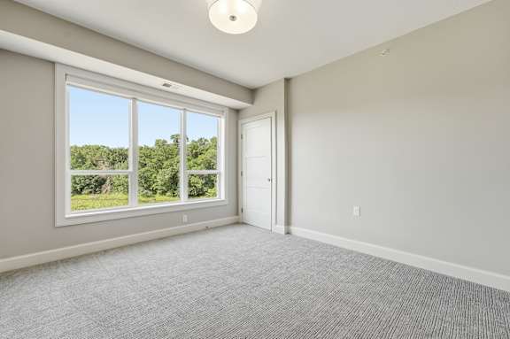 A room with a carpeted floor, a window with a view of trees, and a door.