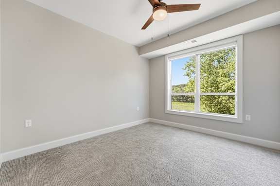 A room with a ceiling fan and a window showing greenery outside.