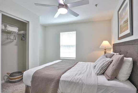 A bedroom with a bed, pillows, a ceiling fan, and a window.
