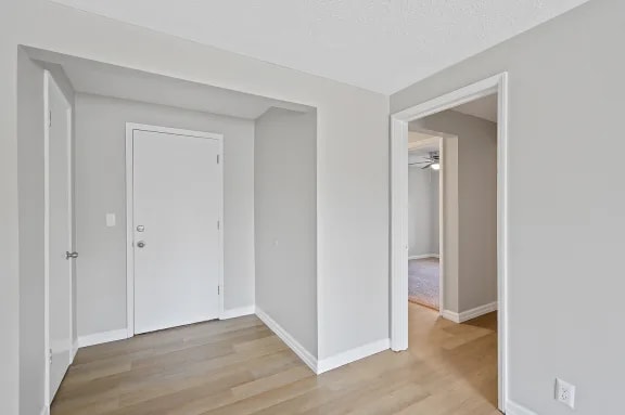 A white door is on the left wall of a room with wood flooring.