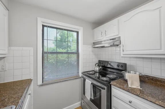 A kitchen with a stove top oven and a window with blinds.