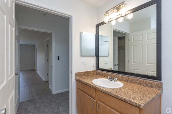 A bathroom with a sink, mirror, and lighting fixture.