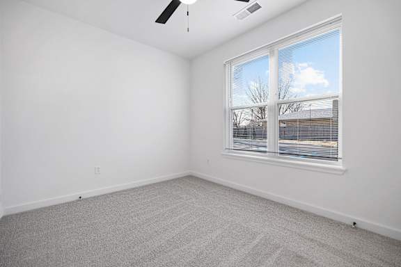 A room with a carpeted floor, a ceiling fan, and a window showing a view of the outside.