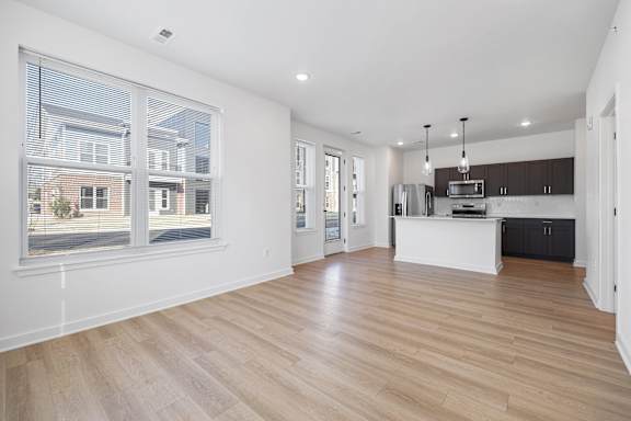 A spacious room with wooden flooring and a kitchen area with black cabinets.