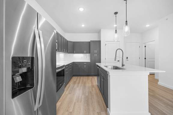 A modern kitchen with a stainless steel refrigerator and wooden flooring.