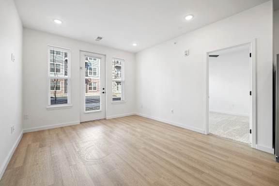 A room with white walls and wooden flooring with three windows.