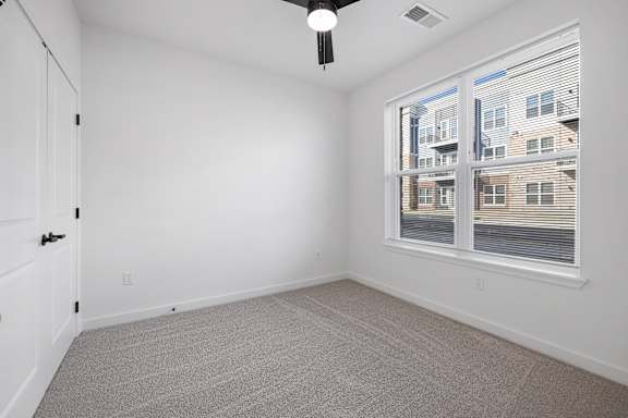 A room with a carpeted floor, a ceiling fan, and a window with blinds.