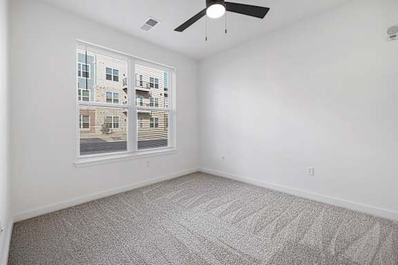 A room with a ceiling fan and a large window overlooking a building.
