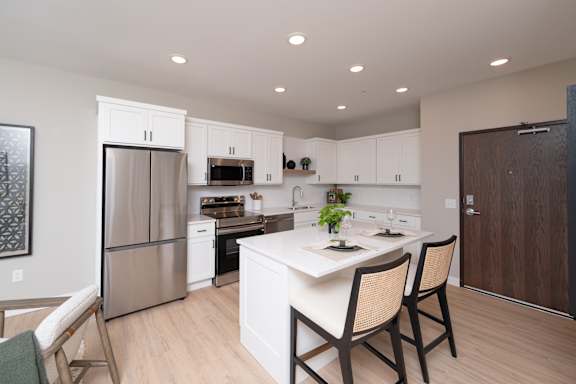 A kitchen with a white island and wooden chairs.