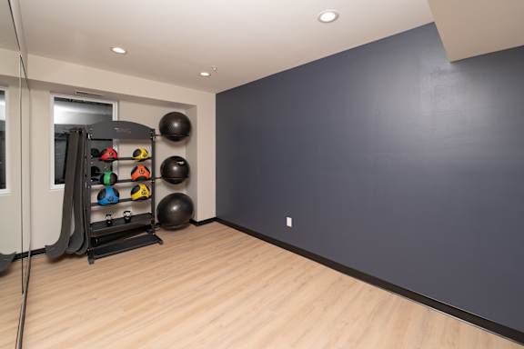 A room with a wooden floor and a wall-mounted rack holding exercise equipment.