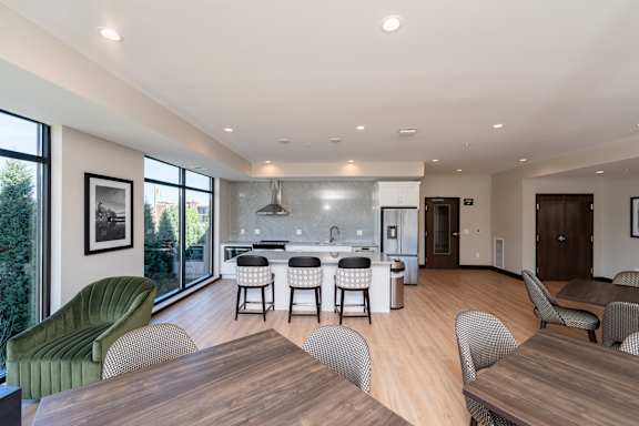 A modern community room kitchen with a dining table, comfortable chairs and shuffle board game.