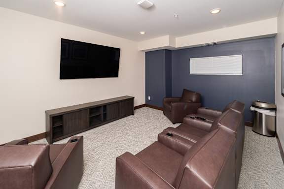 A room with brown leather chairs and a flat screen TV mounted on the wall.