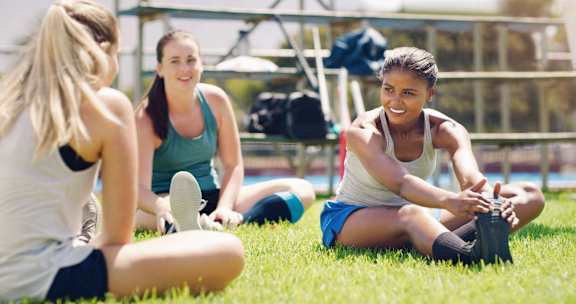 Three women are sitting on the grass, one of them is tying her shoelaces.