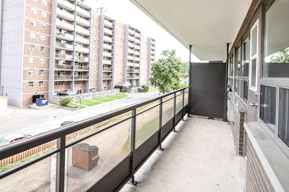A balcony with a black railing and a view of a parking lot and apartment buildings.