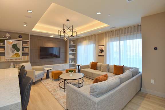 A modern living room with a large grey sofa, a black chair, a coffee table, and a television at Roxy Apartments, Ontario, L8H 0B7