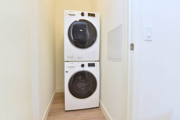 A white front loading washing machine in a narrow hallway at Roxy Apartments, Hamilton, ON