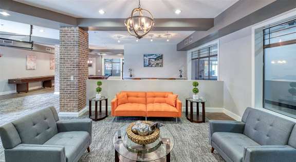 Clubhouse with grey chairs, an orange sofa, and a glass coffee table at Embry Hills, Atlanta, 30042