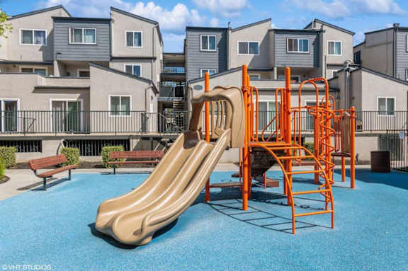 A playground with a slide and swings in front of apartment buildings.