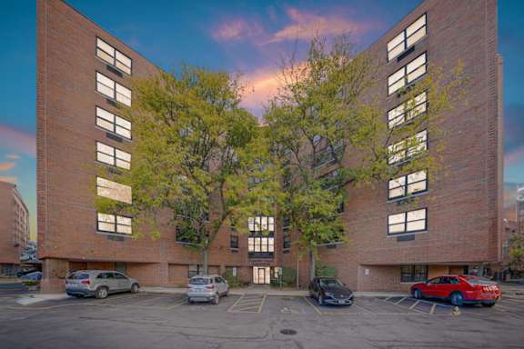 A parking lot in front of a red brick building with cars parked.