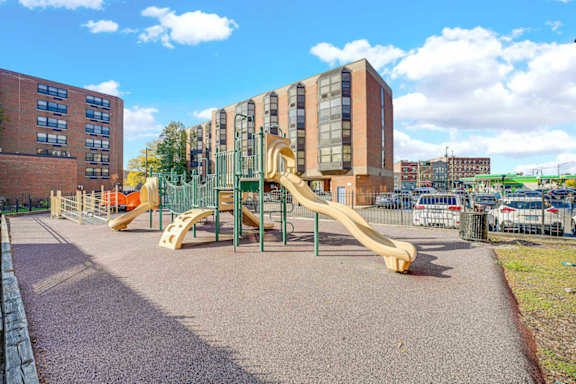 A playground with a yellow slide in front of a building.