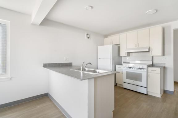 A kitchen with white appliances and a wooden floor.