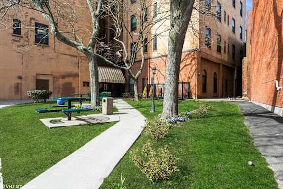 A park with a bench and a tree in front of a brick building.