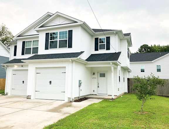 A white house with a black roof and two garages.