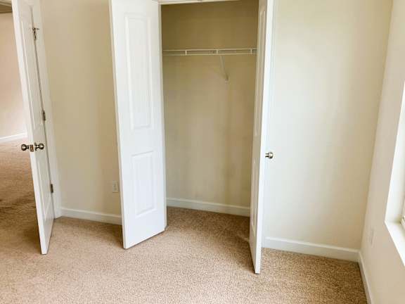A white closet with a door open and a coat hanger.