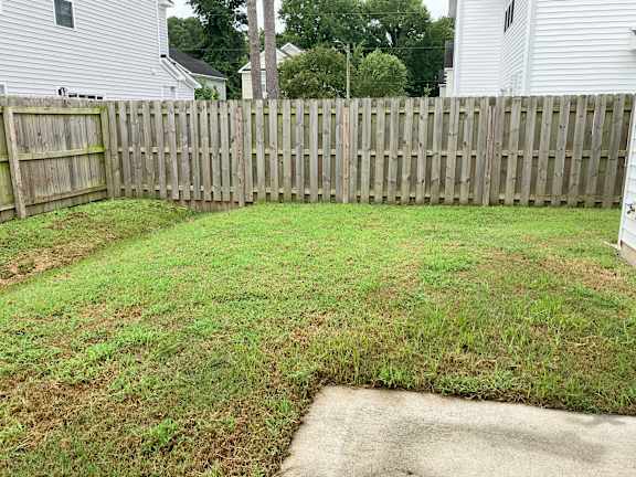 A backyard with a wooden fence and a concrete path.