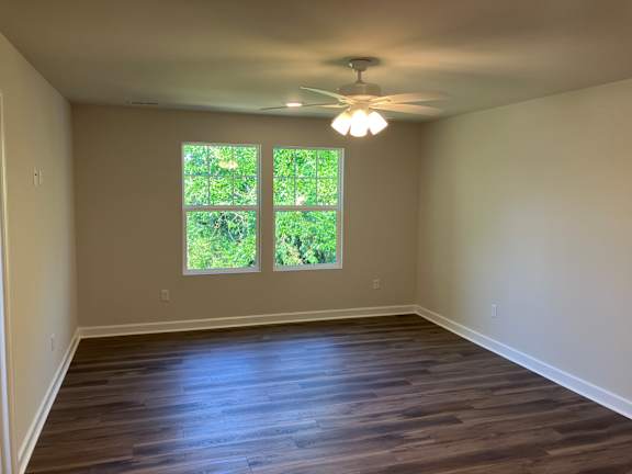 A room with a ceiling fan and two windows.